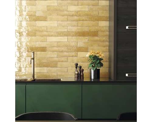 Köksscen med gula kakelplattor, diskho, kran, kryddkvarn och krukväxt.