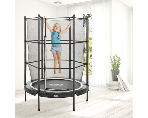 Flicka hoppar på en Salta studsmatta med säkerhetsnät i ett ljust rum.