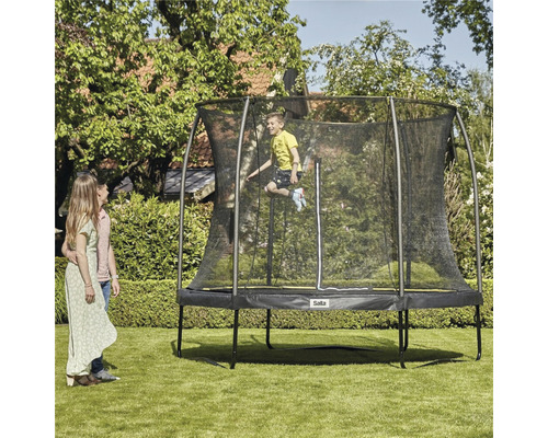 Familj med rund trädgårdstrampolin med säkerhetsnät och hoppande barn i trädgården.