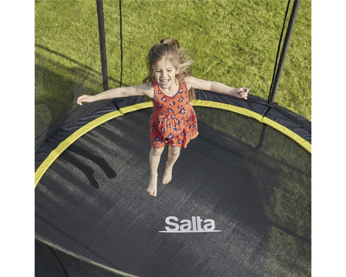 En flicka hoppar på en rund Salta-trädgårdstrampolin.