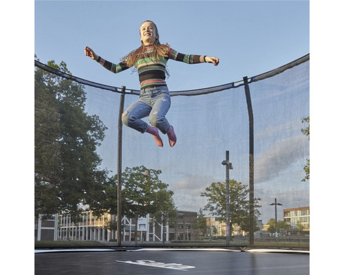 Flicka hoppar på en studtrampolin med säkerhetsnät