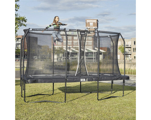 Flicka hoppar på rektangulär trädgårdstrampolin med säkerhetsnät.