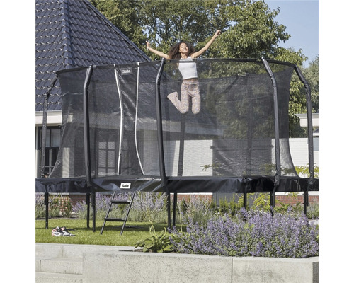 Svart trädgårdstrampolin med säkerhetsnät och stege i trädgården med hoppande person