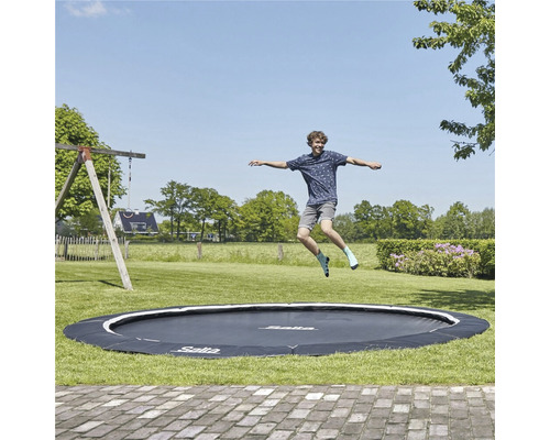 En man hoppar på en rund Salta-trampolin i trädgården.