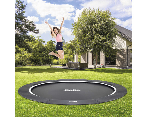 En kvinna hoppar på en rund Salta trädgårdstrampolin med säkerhetskant.