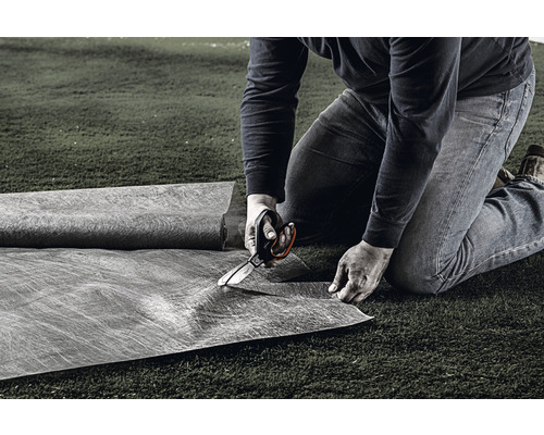 En person klipper ogräsduk med en sax på en gräsmatta.