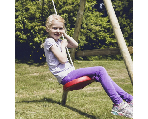 Flicka gungar på en rund gunga i trädgården.