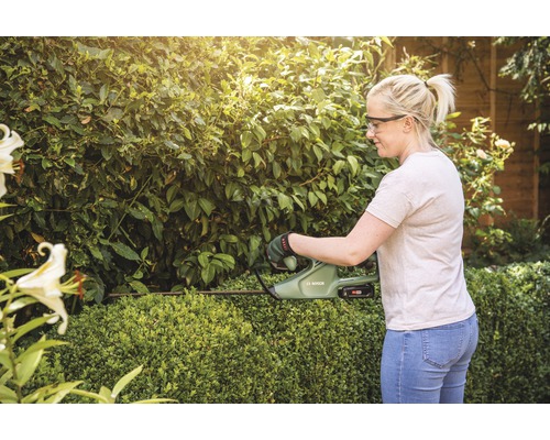 Kvinna klipper häck med en batteridriven häcksax