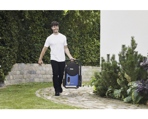 En man bär en bärbar högtryckstvätt i trädgården.