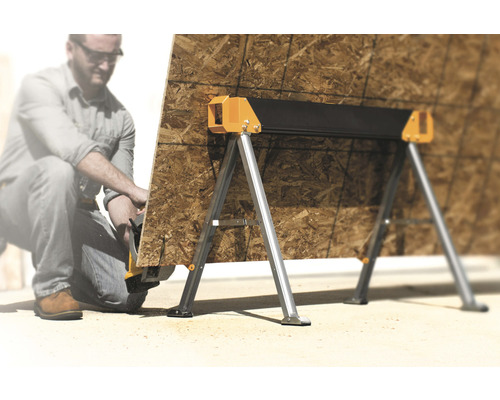 Två sågbockar i metall med en träplanka och en person i bakgrunden.