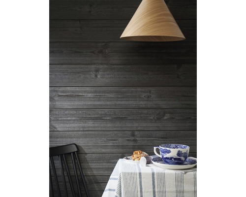 Hängande trälampa ovanför ett bord med porslin och en svart stol framför en träpanel