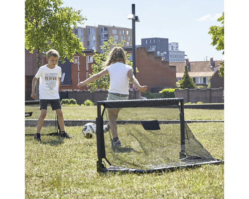 Två barn leker med ett fotbollsmål på en gräsmatta.