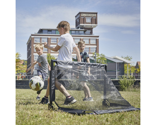 Tre barn leker med ett fotbollsmål på en gräsmatta.