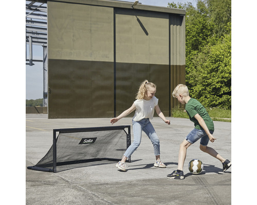 Två barn spelar med ett Salta fotbollsmål på en plats.