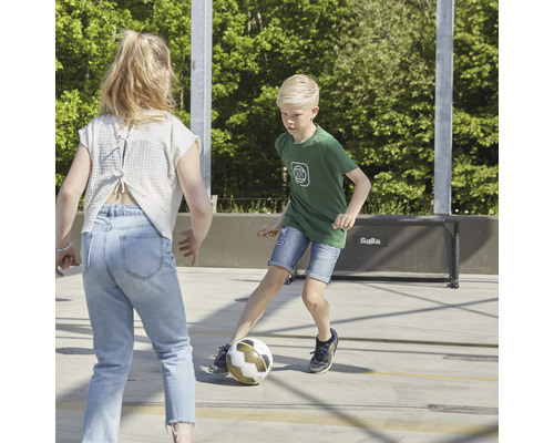Två barn leker med en fotboll på en idrottsplats med ett mål.