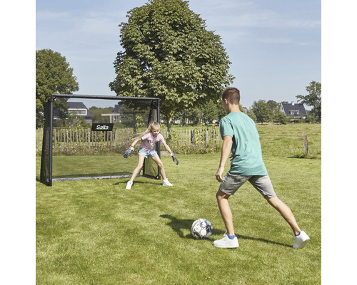 Trädgårdsscen med två barn som spelar fotboll, med ett Salta fotbollsmål.