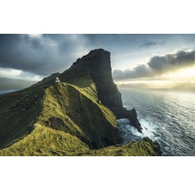 Landskap med en fyr på en grön klippa vid havet under en molnig himmel.