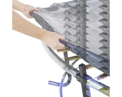 Närbild av en studsmatta med fjädrar och ett skydd som hålls av en hand.