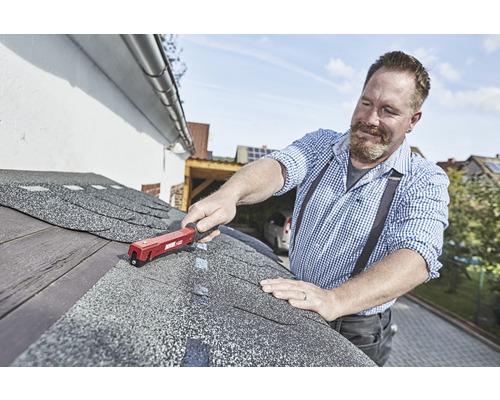 Hantverkare fäster bitumenshingel med en takpappspikare på ett tak.