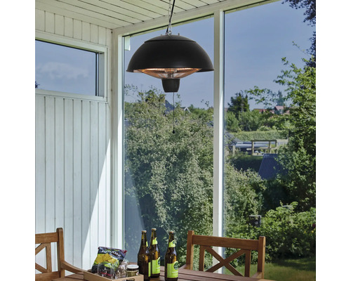Miljöbild med en hängande lampa och en terrassvärmare ovanför ett träbord med drycker och snacks