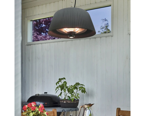Mörk terrassvärmare med lampskärm hänger ovanför ett bord på en terrass.