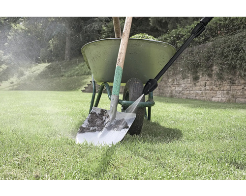 Rengöring av en spade med en högtryckstvätt bredvid en skottkärra på en gräsmatta