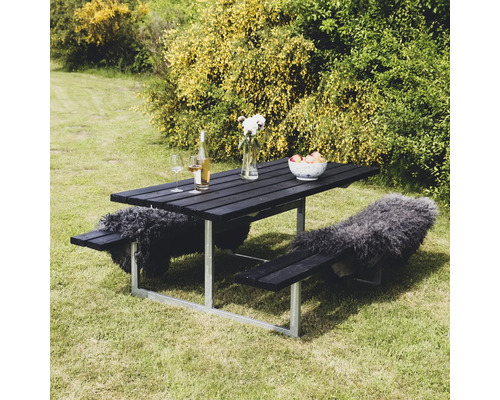 Svart picknickbordsset i trä med stålram, dekorerad med drycker, blomvas, fruktskål och skinn i trädgården.