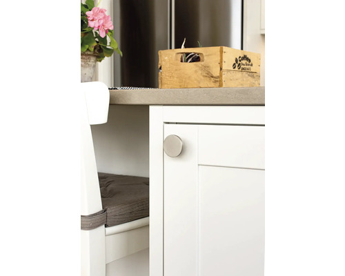 Detaljvy av ett köksskåp med ett runt metallhandtag, en trälåda och en bänk med kudde