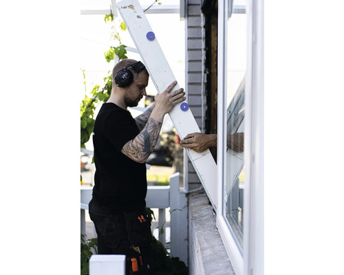 Man med hörselskydd monterar en träskiva på ett fönster