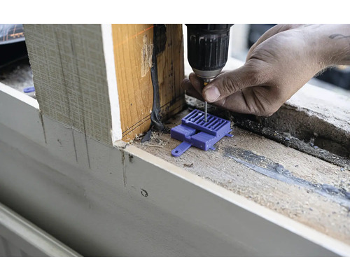En hantverkare borrar en skruv i en fönsterkarm med en batteridriven skruvdragare med hjälp av ett monteringshjälpmedel.