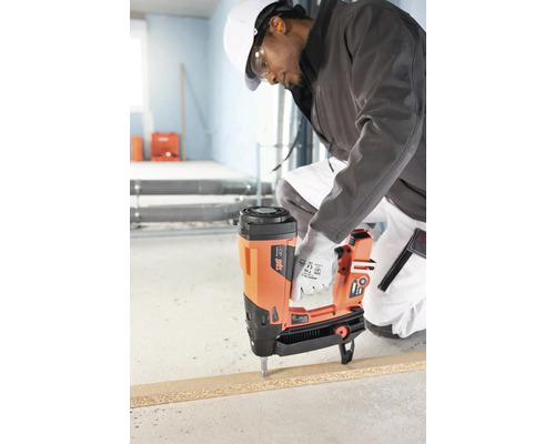 En byggnadsarbetare fäster ett arbetsstycke med en bultpistol.