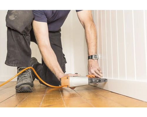 Hantverkare fäster en golvsockel med en pneumatisk spikpistol.