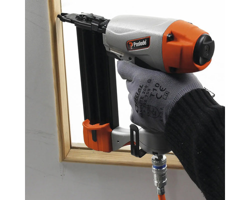 En person använder en tryckluftsdriven spikpistol för att fästa dekorativa lister.