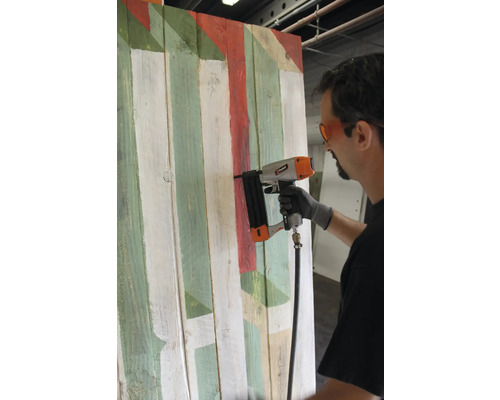 Man använder pneumatisk häftpistol på färgad trävägg