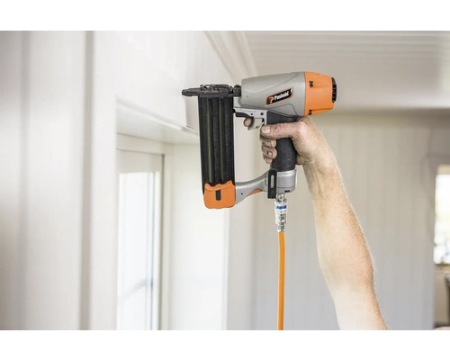 En person använder en pneumatisk häftpistol på en vit vägg.