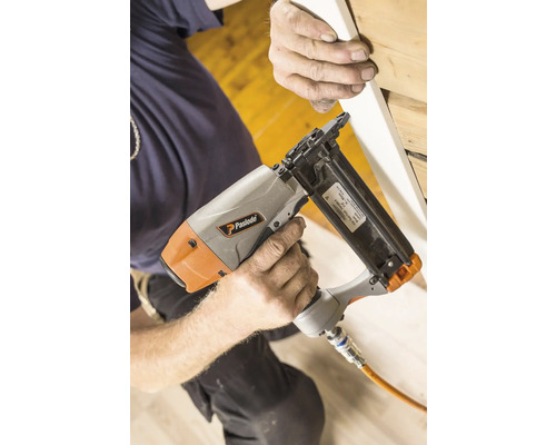 En person fäster en list på en vägg med en pneumatisk spikpistol. Paslode logotypen är synlig.