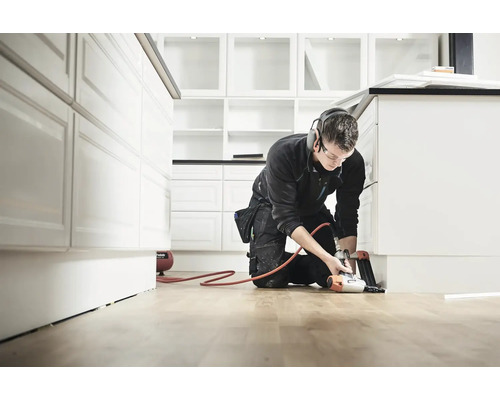 Hantverkare monterar golvlister med en pneumatisk spikpistol i ett kök.