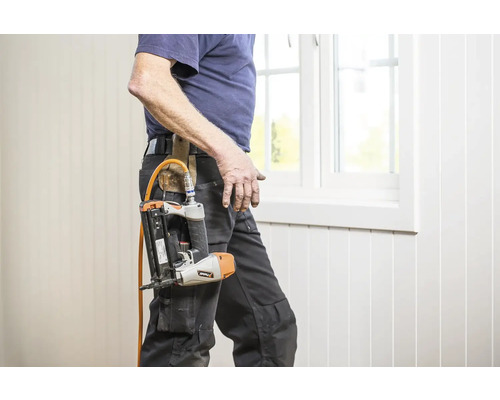 Hantverkare med tryckluftsdriven spikpistol i bältet nära ett fönster