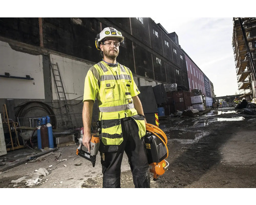 En byggnadsarbetare bär skyddskläder och verktyg på en byggarbetsplats.