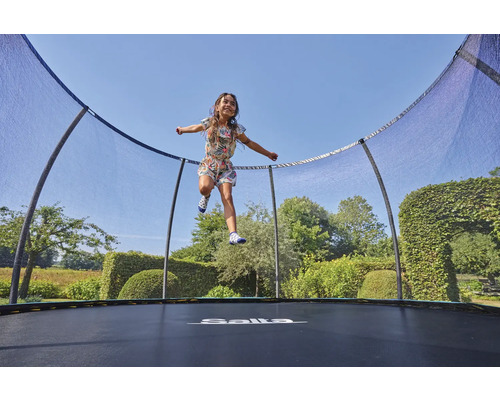 Flicka hoppar på en trädgårdstrampolin med skyddsnät. Märke Salta.