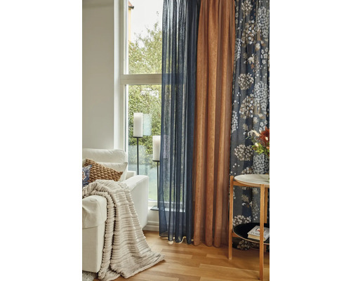 Vardagsrum med soffa, bord och fönster med gardiner i olika färger och mönster.