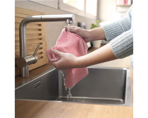 En person tvättar en trasa i en diskho i rostfritt stål under en kran.