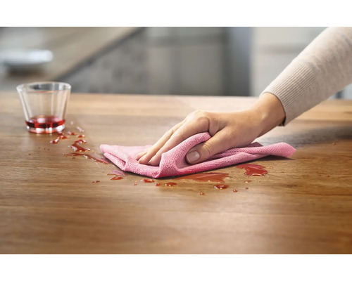 En person torkar upp spilld vätska från ett bord med en trasa.
