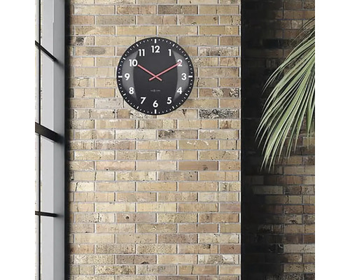 Svart väggklocka med röd visare framför en tegelvägg