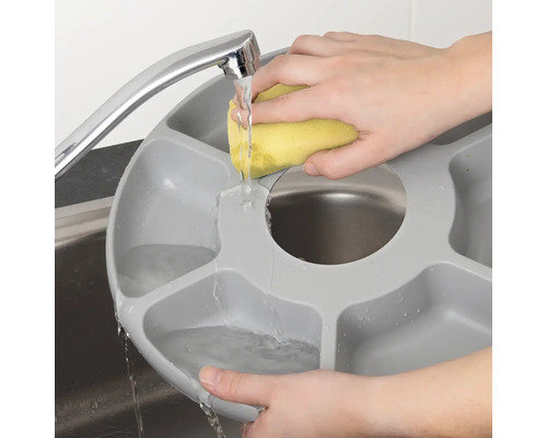 En person diskar en grå diskbalja med fack under en kran med en svamp