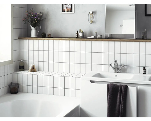 Ljust badrum med vitt kakel, handfat och förvaringsutrymme