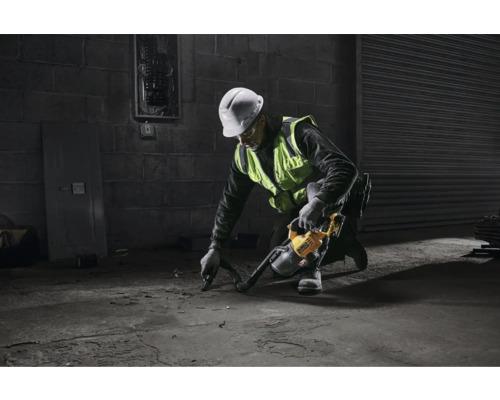 En man med skyddshjälm och varselväst använder en industridammsugare på ett betonggolv.