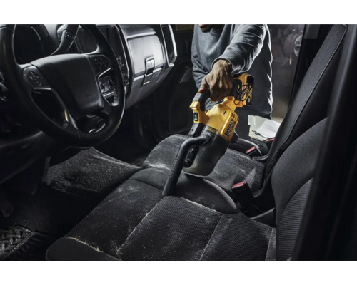 En person dammsuger insidan av en bil med en gul DeWalt handdammsugare.