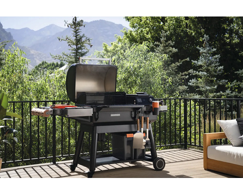 Öppen kolgrill på en uteplats med räcke och utsikt över ett grönt landskap