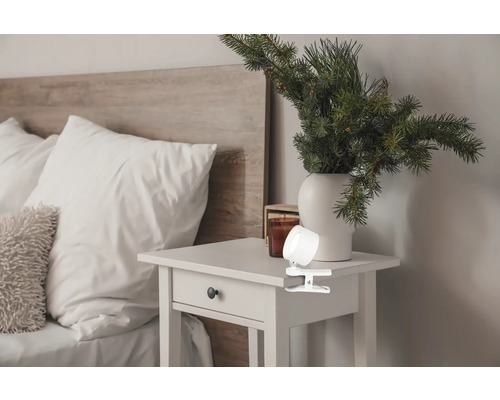 Klämlampa på ett sängbord bredvid en säng med sänggavel